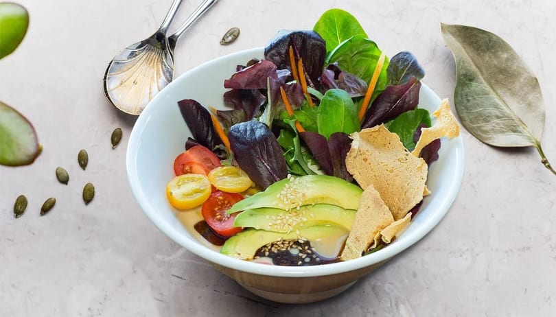 Colorful salad with mixed greens, cherry tomatoes, avocado, and sesame seeds in a white bowl.