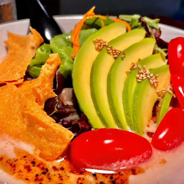 Close-up of a vibrant salad with sliced avocado, cherry tomatoes, greens, and crispy wonton strips.