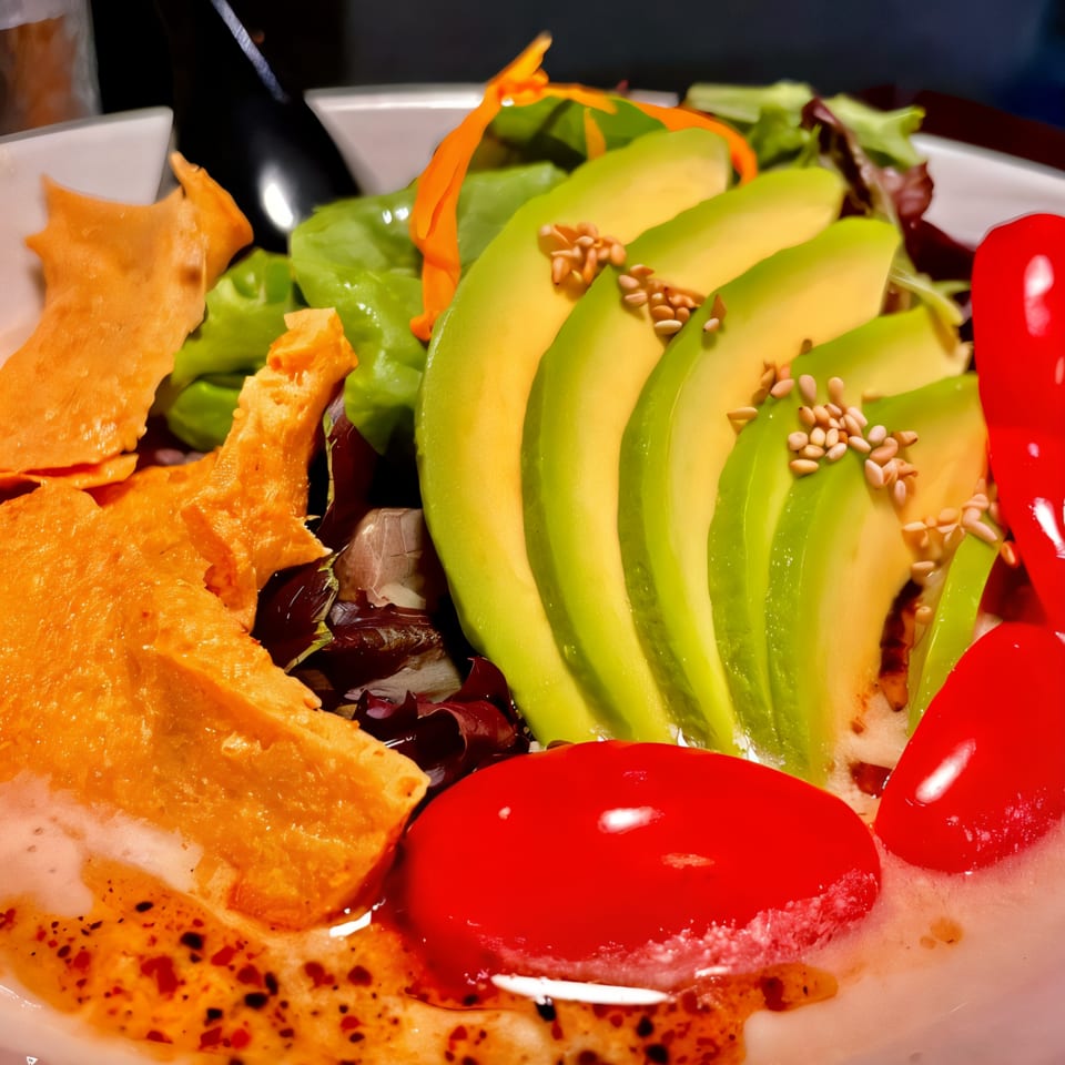 Close-up of a vibrant salad with sliced avocado, cherry tomatoes, greens, and crispy wonton strips.