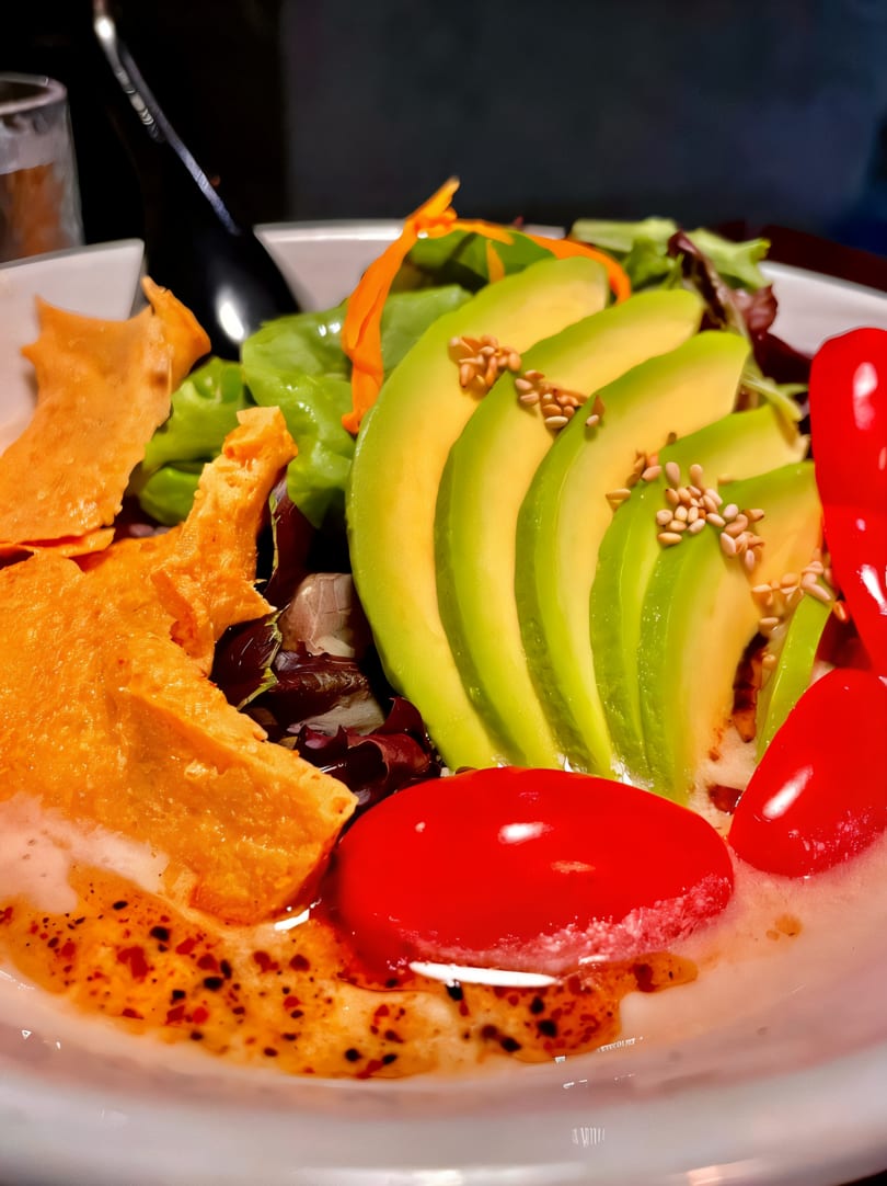 Close-up of a vibrant salad with sliced avocado, cherry tomatoes, greens, and crispy wonton strips.
