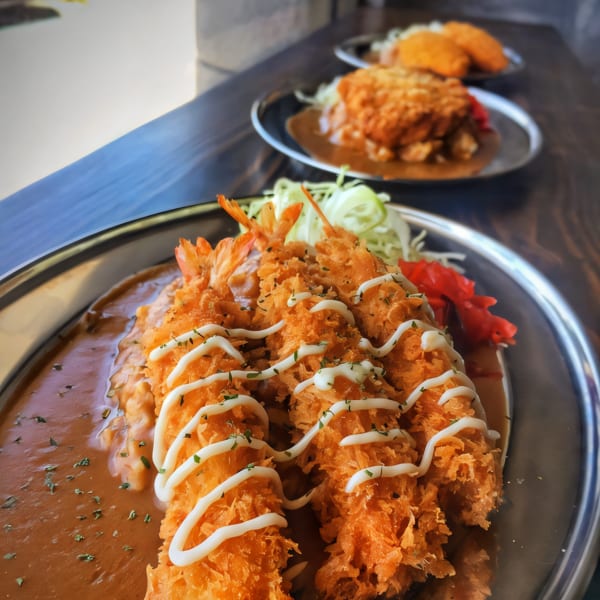 Three plates of Japanese curry with fried shrimp and cutlets, garnished with mayonnaise and herbs.