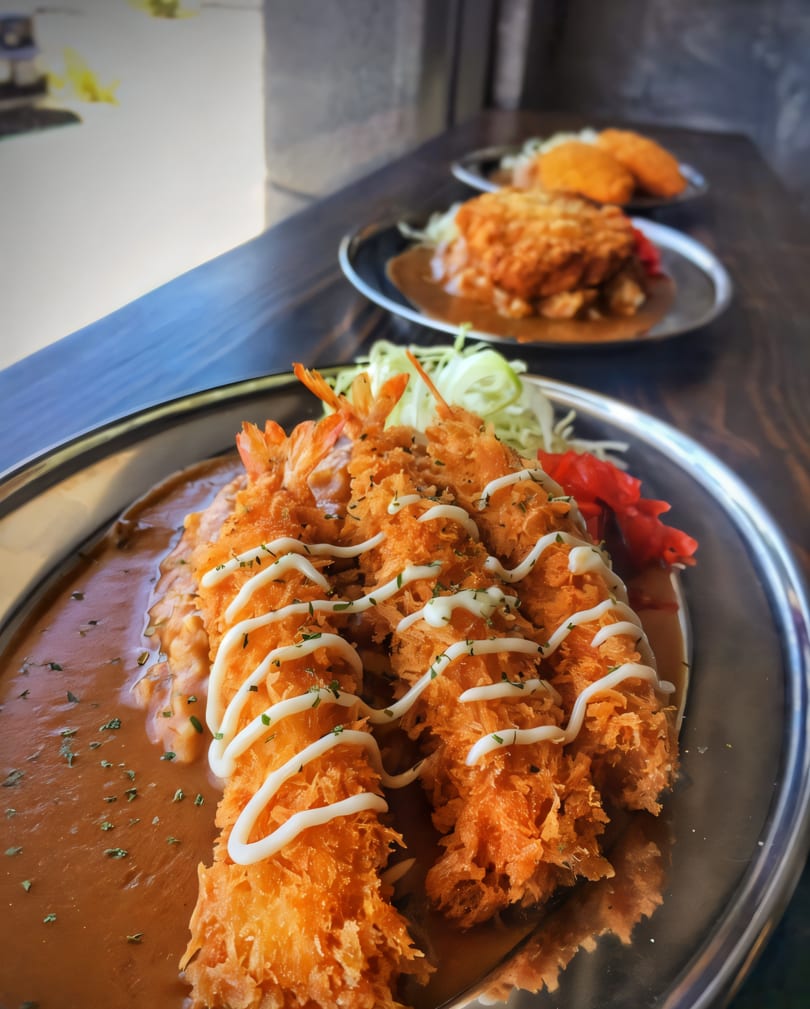 Three plates of Japanese curry with fried shrimp and cutlets, garnished with mayonnaise and herbs.