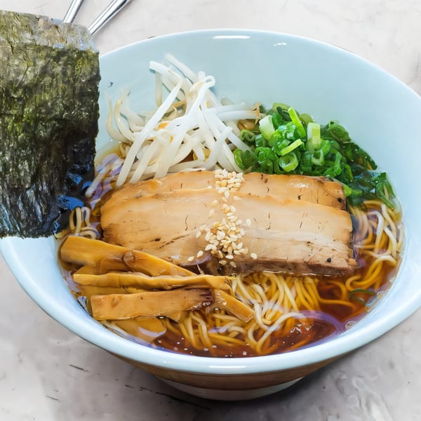 A light blue bowl of ramen with pork, bamboo shoots, scallions, bean sprouts, and nori.